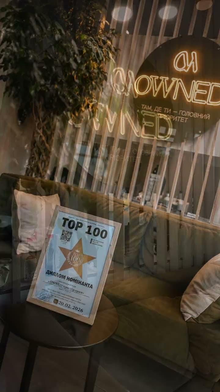 Зал OWNED: оливковий диван, підсвічена вивіска та диплом TOP 100 на столику